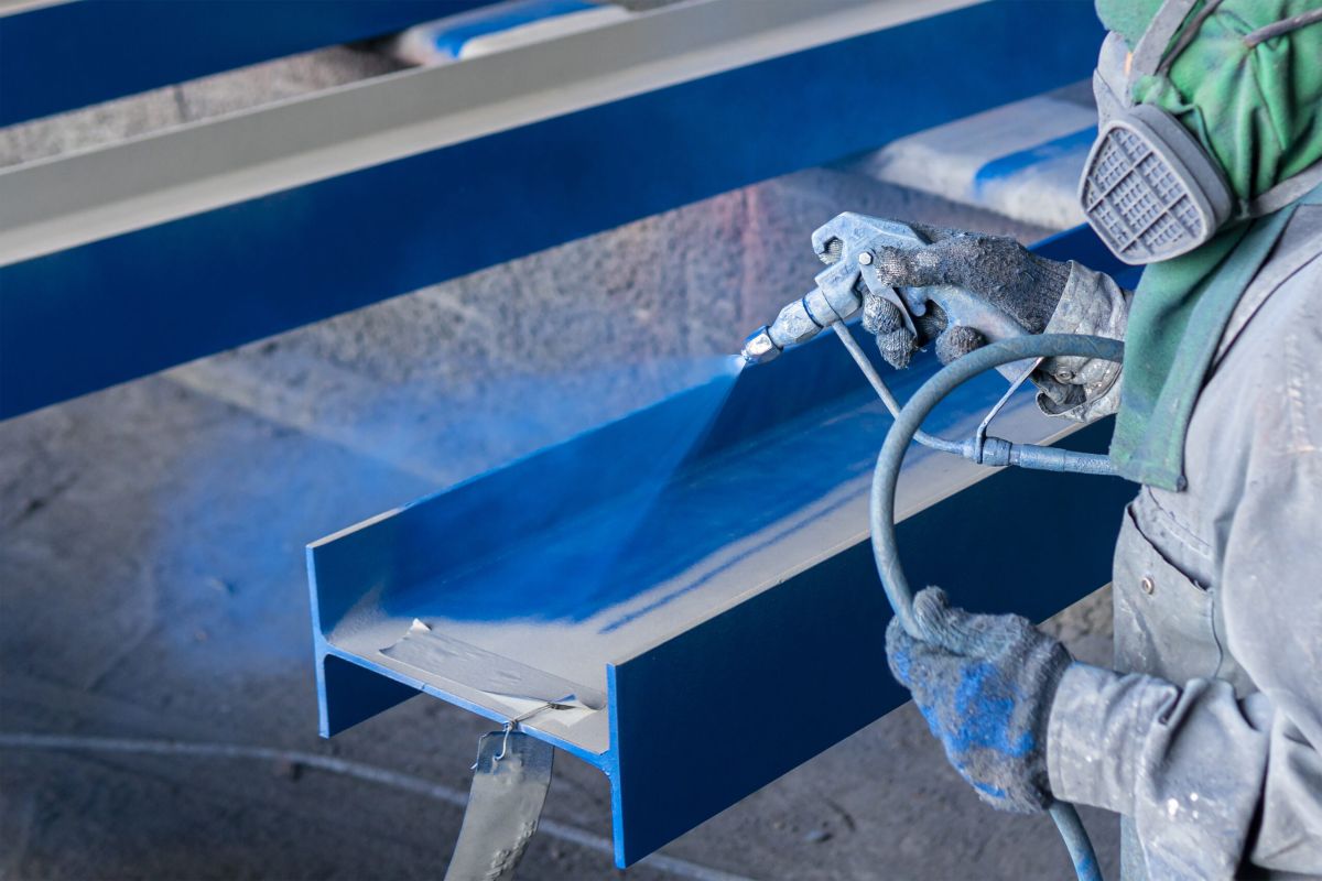 Painting color top coat on steel structure with spray gun at industrial factory.